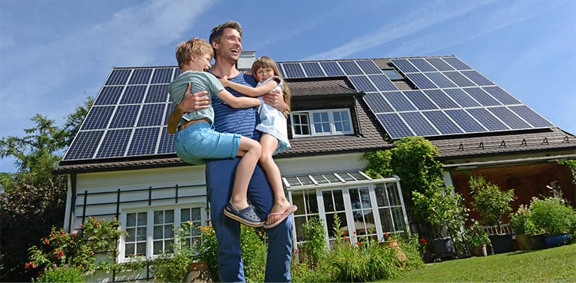 Father carrying two happy children in front of their sustainable house